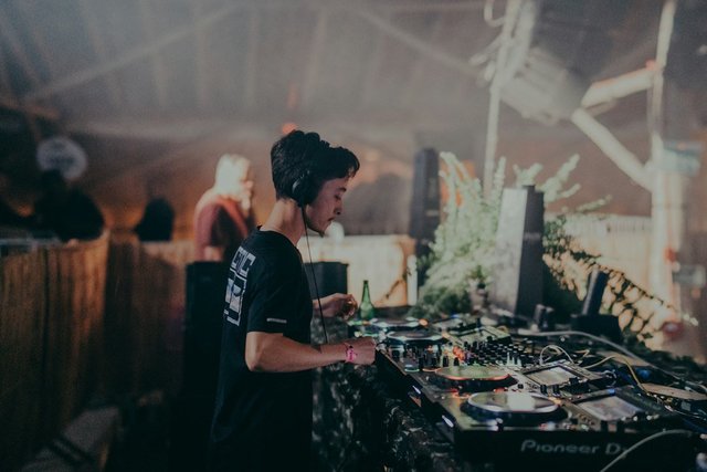 A DJ working at a mixing console under warm lighting at a live electronic music event