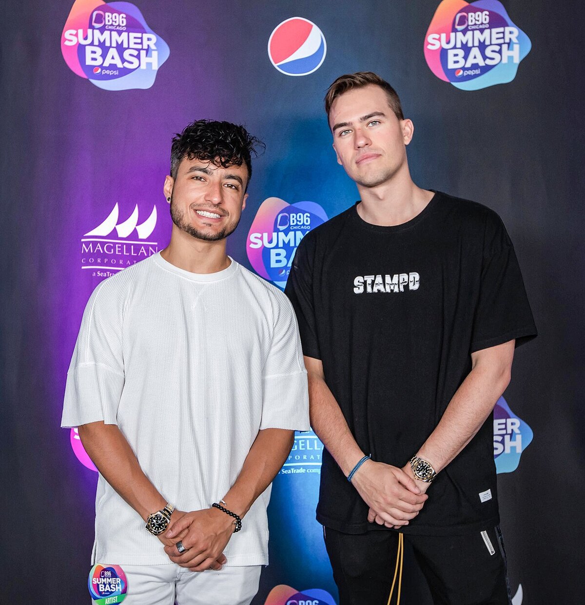 Two members of the dance duo Loud Luxury posing together in front of a festival sponsor backdrop