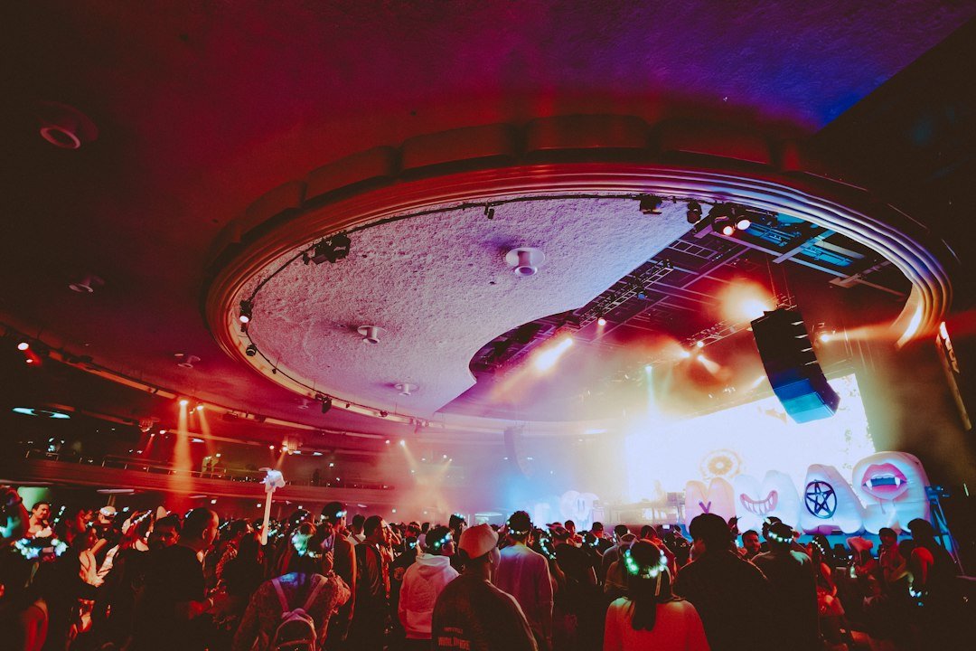 A crowd illuminated by colorful stage lights at a nighttime DJ set in a club venue