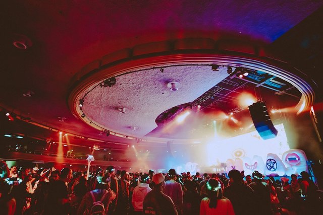 A crowd illuminated by colorful stage lights at a nighttime DJ set in a club venue