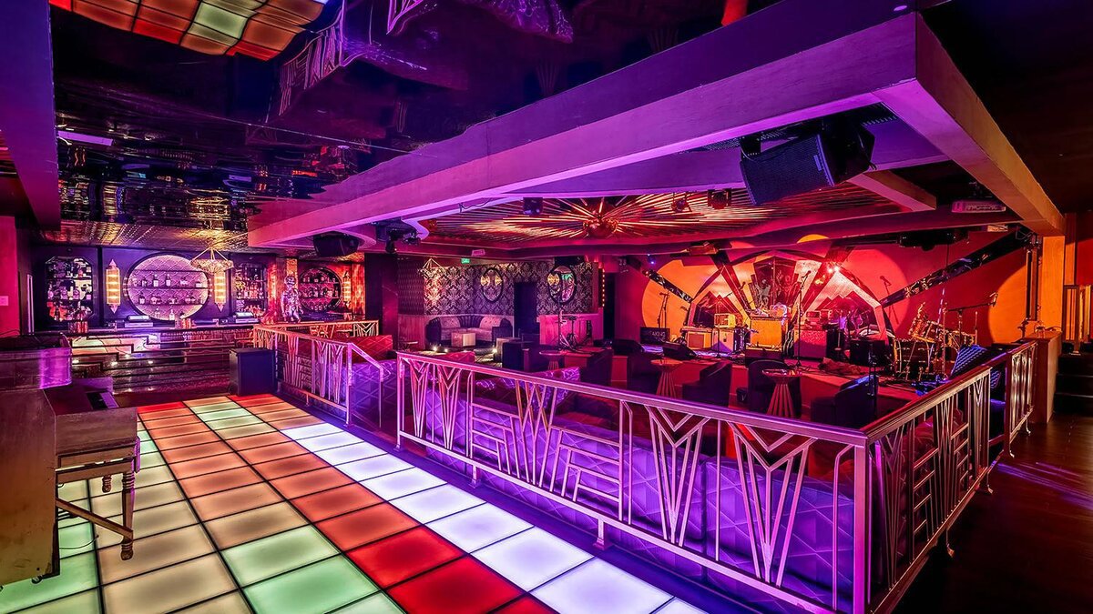 Colorful lit dance floor and lounge area with a stage in the background inside a Los Angeles nightclub