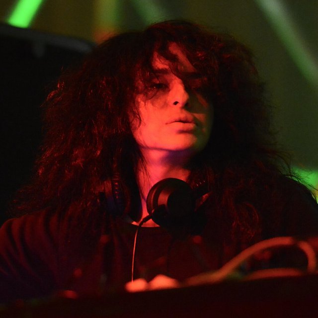 Nicole Moudaber at a DJ booth under red and green stage lighting, headphones around her neck