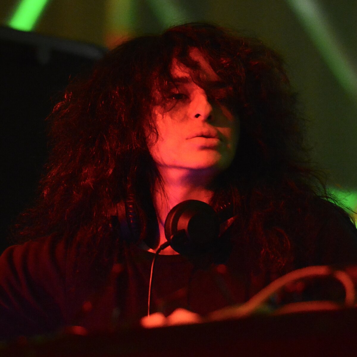 Nicole Moudaber at a DJ booth under red and green stage lighting, headphones around her neck