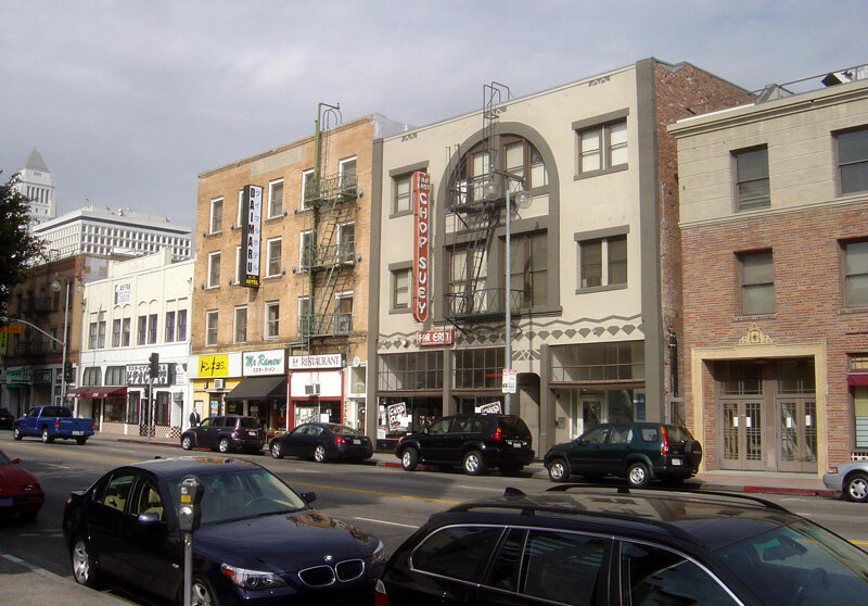 Little Tokyo storefronts and vertical signs on a downtown Los Angeles street, with a tall civic tower behind