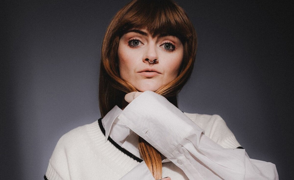 Ninajirachi in a close promo portrait wearing a white jacket with her hand at her chin