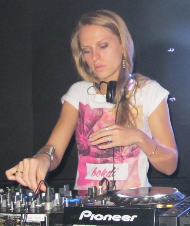 DJ with headphones around her neck working a Pioneer mixer in a dark club