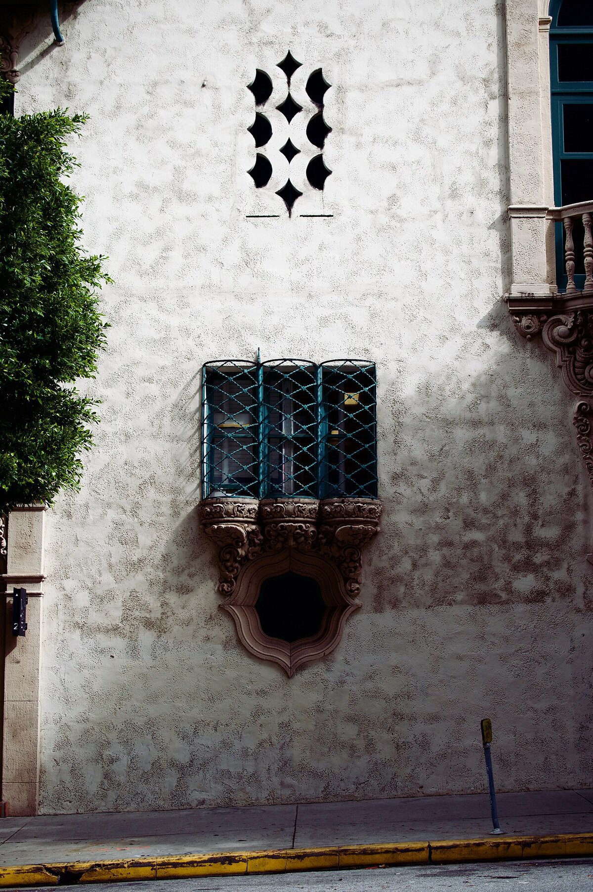 Ornate Spanish Revival wall with a barred window and cutout vents on Wilshire Boulevard in Koreatown