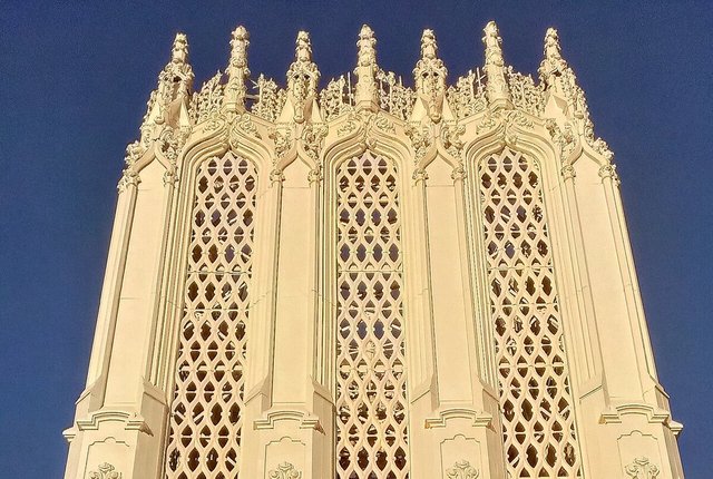 Sunlit Gothic Revival tower and carved terra cotta facade of the building on S Broadway that houses the venue, against a deep blue sky