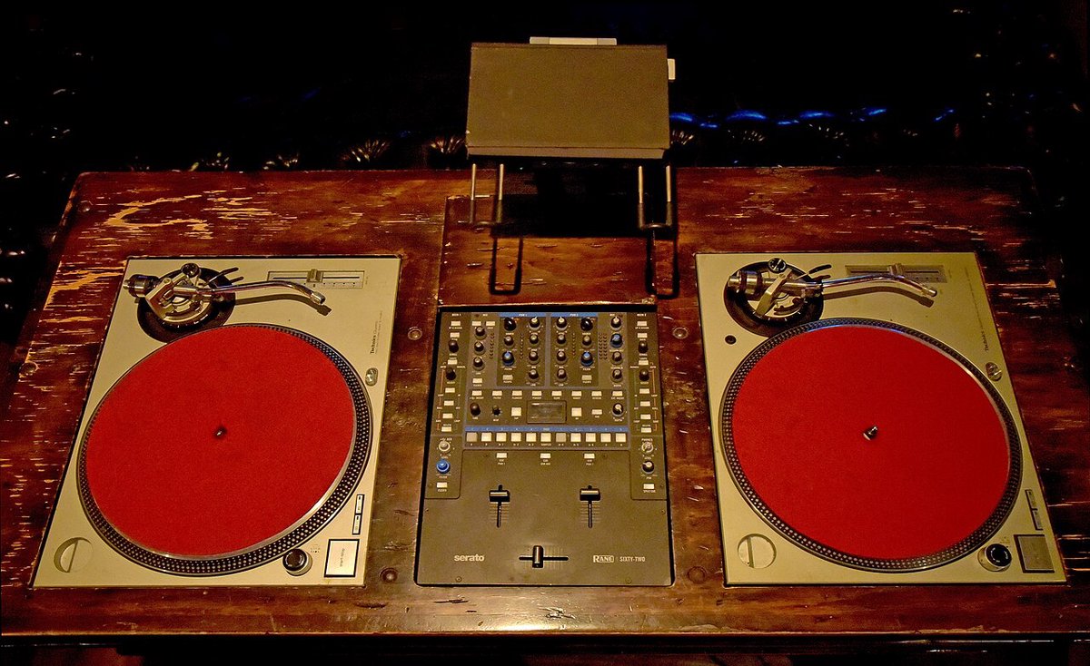 Two red-platter turntables and a mixer on a wooden DJ station