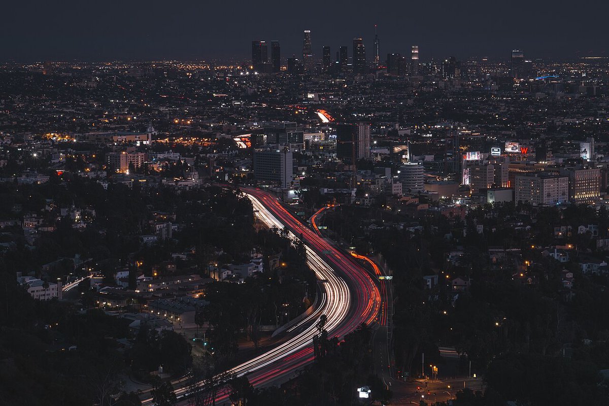 Red and white light trails along a Los Angeles freeway at night with the downtown skyline in the distance
