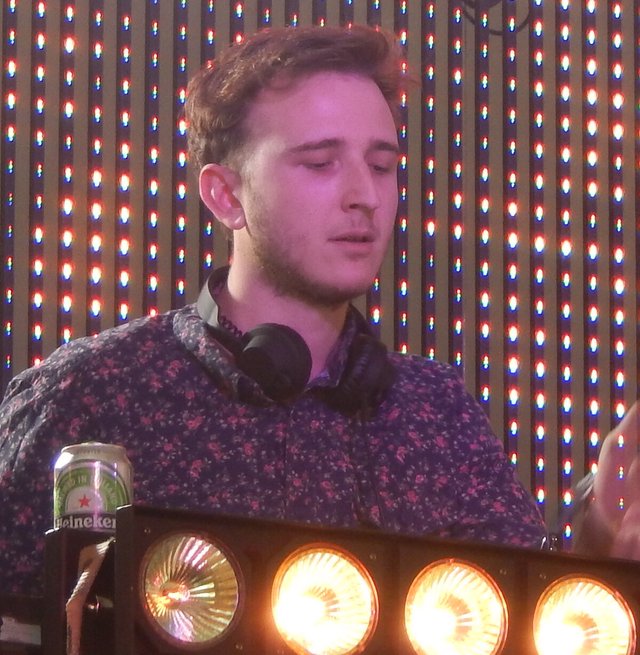DJ with headphones around his neck standing at a booth in front of a wall of LED lights