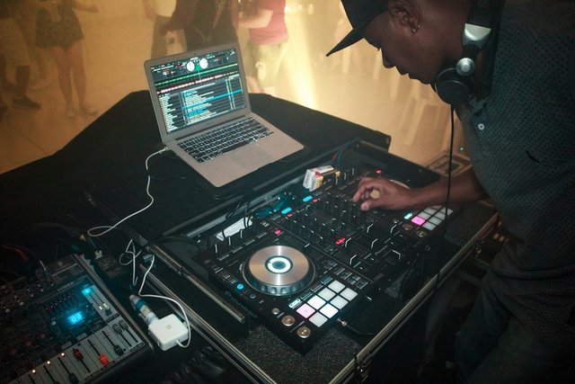 A DJ in a black shirt performing a late-night set under warm stage lighting at a club venue