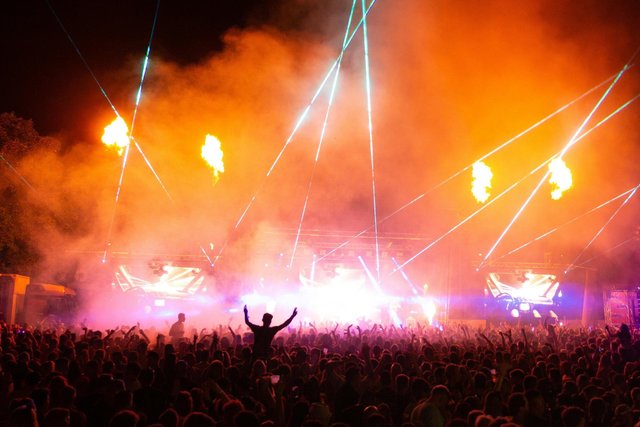 A sunset-lit outdoor festival stage with a crowd gathered in front