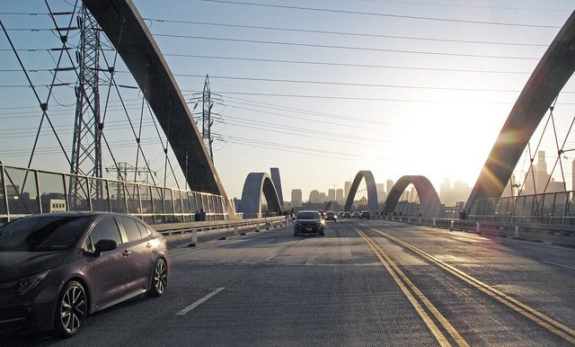 Sunlit arches of the 6th Street Bridge in Los Angeles with cars on the roadway and the downtown skyline in the haze