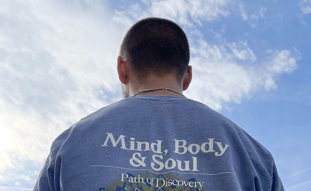 Swimming Paul seen from behind against a blue sky, wearing a faded blue t-shirt printed with Mind, Body and Soul