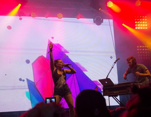 Sylvan Esso performing on stage at a festival, lit from behind