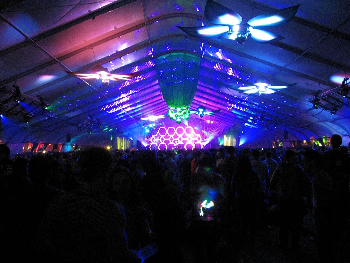 Packed dance tent with laser beams, hexagon stage lighting and hanging flower lights at Beyond Wonderland