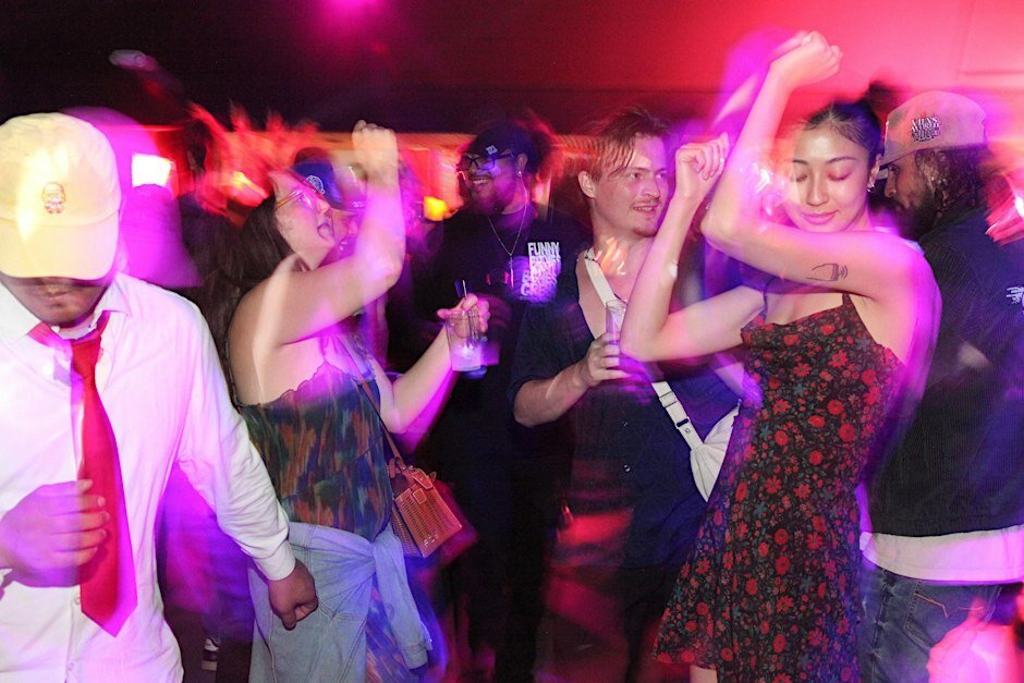 Motion-blurred dancers under pink and purple club lighting, mid-move with drinks in hand