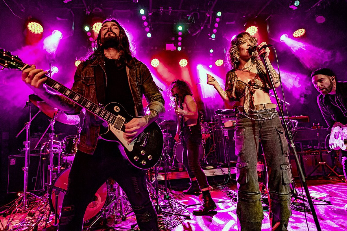 A band playing under magenta and purple stage lights in a ballroom venue