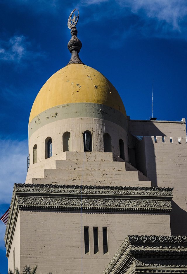 Yellow onion dome and carved stone trim of the Shrine Auditorium against a deep blue sky