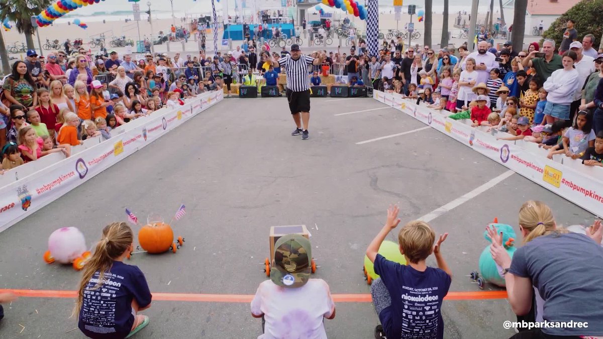 Kids cheering at the starting line of the Manhattan Beach Pumpkin Race as a referee signals and a crowd lines the course