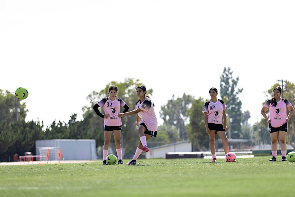 Young players in pink Angel City FC training jerseys warming up with soccer balls on a grass field