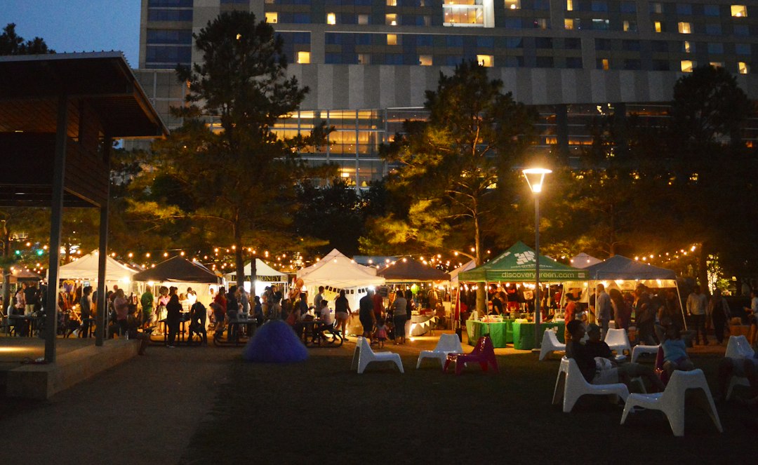 Families gathered under string lights and white vendor tents at an evening outdoor night market