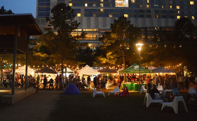 Families gathered under string lights and white vendor tents at an evening outdoor night market