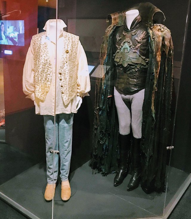 Two display cases with costumes from the film Labyrinth, a ruffled white shirt and vest beside a dark armored coat and cape