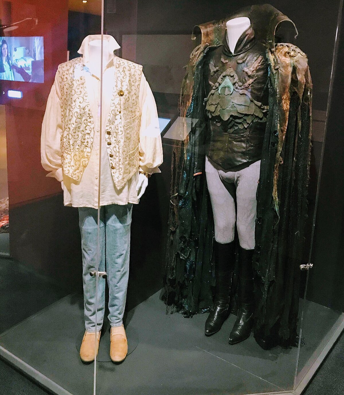 Two display cases with costumes from the film Labyrinth, a ruffled white shirt and vest beside a dark armored coat and cape