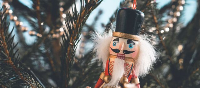 Wooden nutcracker ornament with a black hat and white beard hanging among pine branches