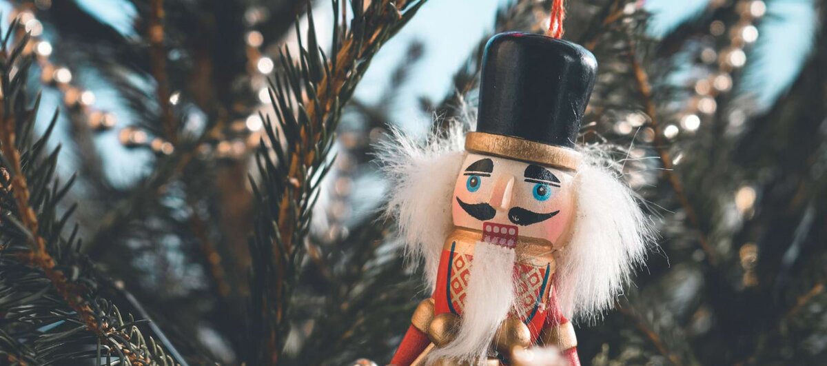Wooden nutcracker ornament with a black hat and white beard hanging among pine branches