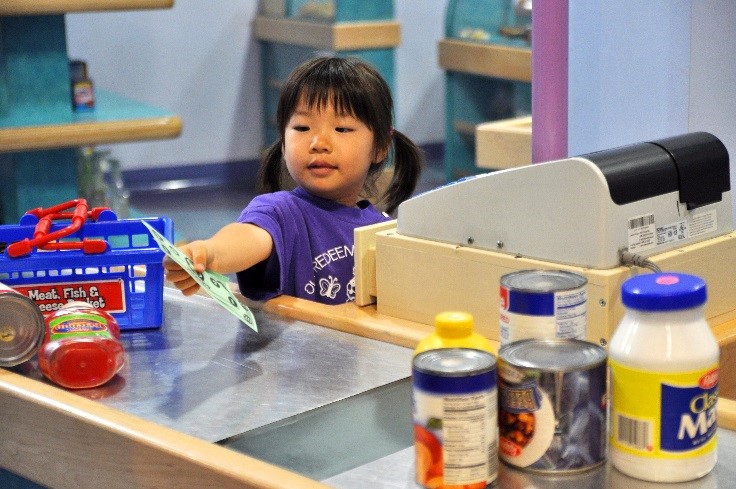 A young girl plays cashier at the pretend grocery store checkout inside Pretend City Children's Museum