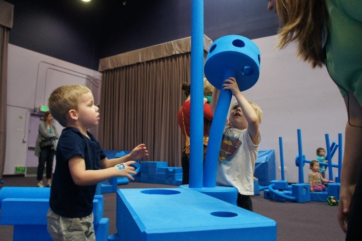 Two young boys build with oversized blue foam blocks and poles in the Imagination Playground room at Pretend City Children's Museum