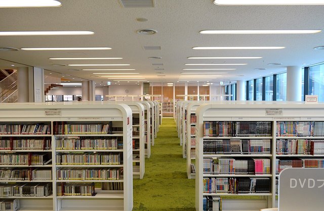 A bright open library floor with long rows of low white bookshelves
