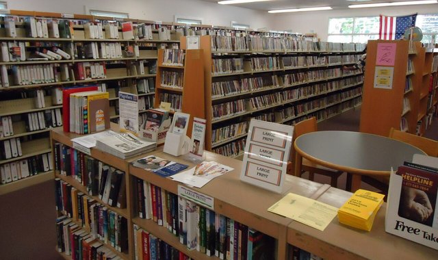 Library shelves of books with a reading table and displays in the foreground