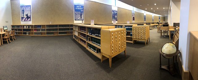 An empty library reading room with low shelving, a card catalogue and a globe under a long ceiling