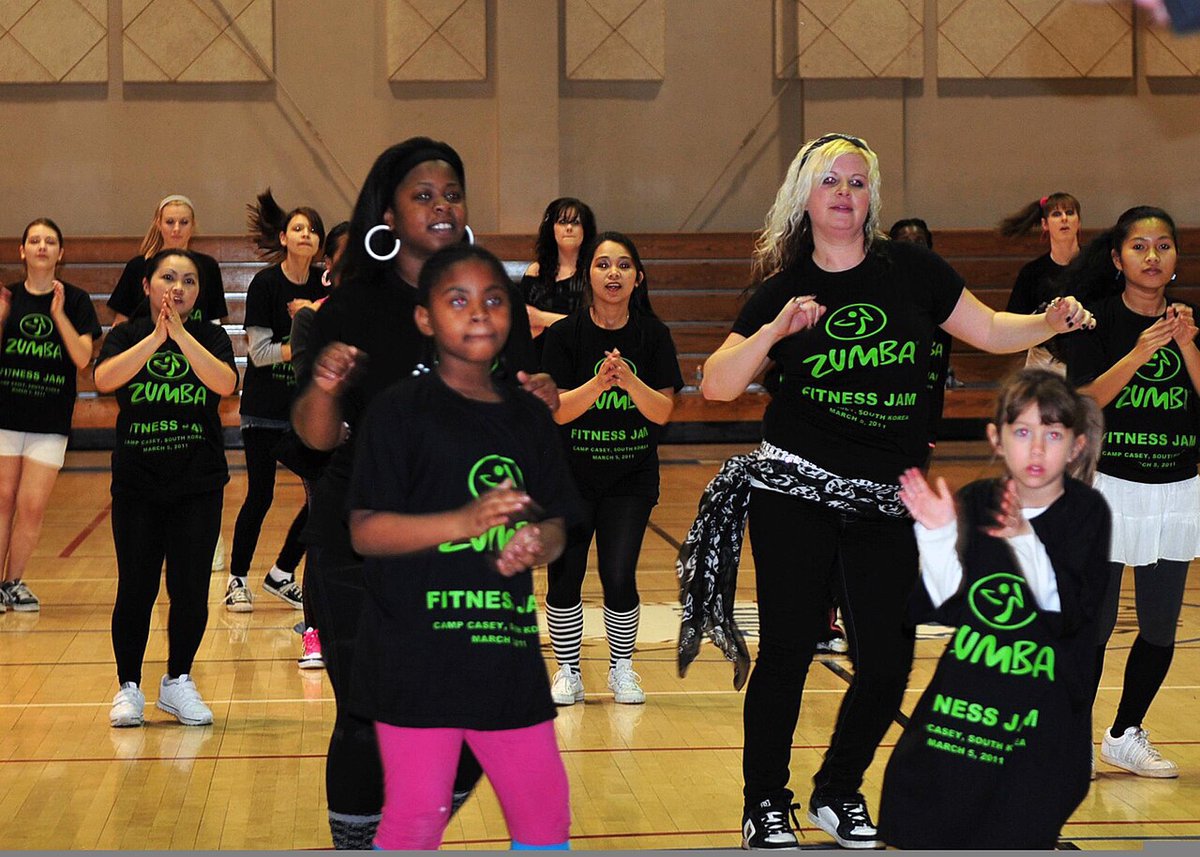 Kids and adults in matching Zumba T-shirts following a dance routine on a gym floor