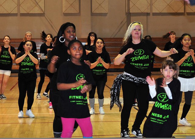 Kids and adults in matching Zumba T-shirts following a dance routine on a gym floor