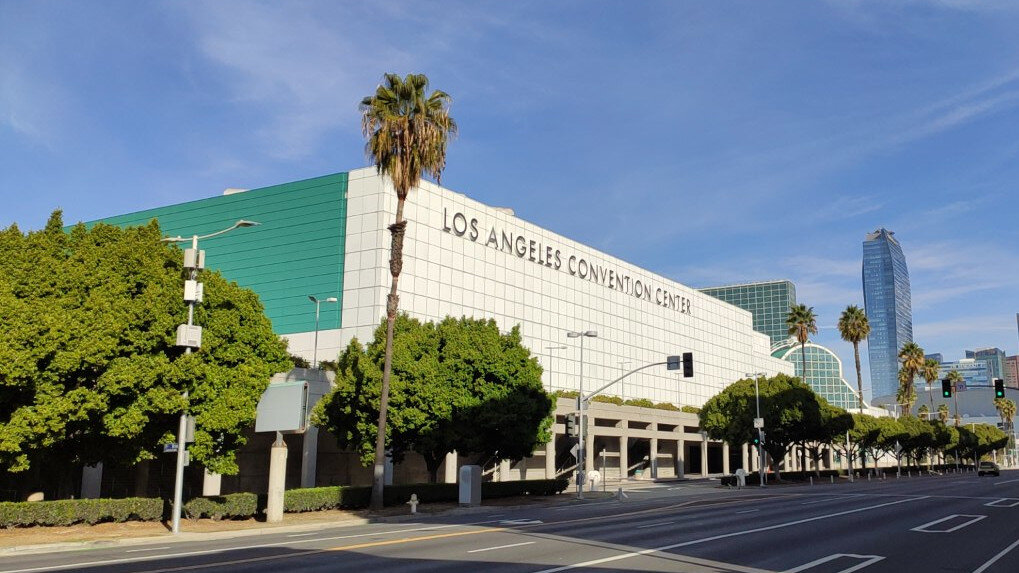 Exterior of the Los Angeles Convention Center with palm trees and downtown towers behind it