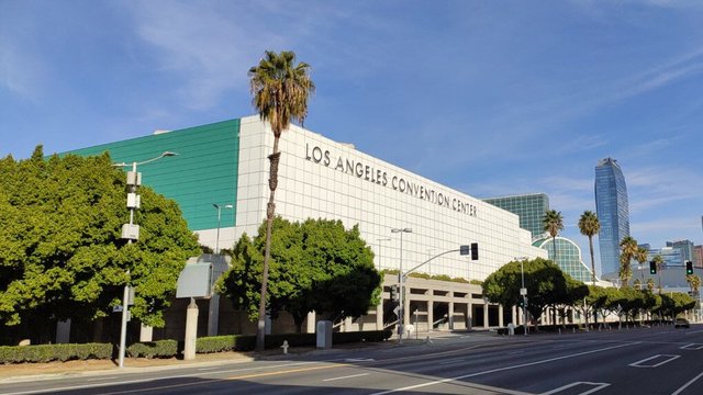 Exterior of the Los Angeles Convention Center with palm trees and downtown towers behind it