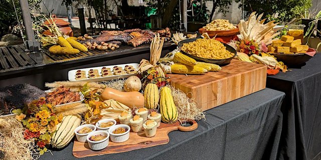 Harvest-style food table with grilled meats, corn, squash and desserts at an outdoor event