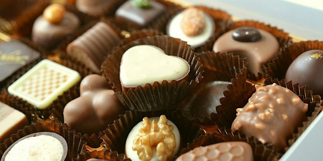 A box of assorted filled chocolates in paper cups, including a white chocolate heart and a walnut-topped bonbon
