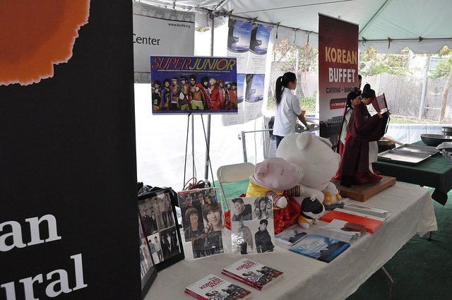 A Korean cultural booth under a festival tent at Seoul International Park, with K-pop posters, books and a figure in traditional hanbok