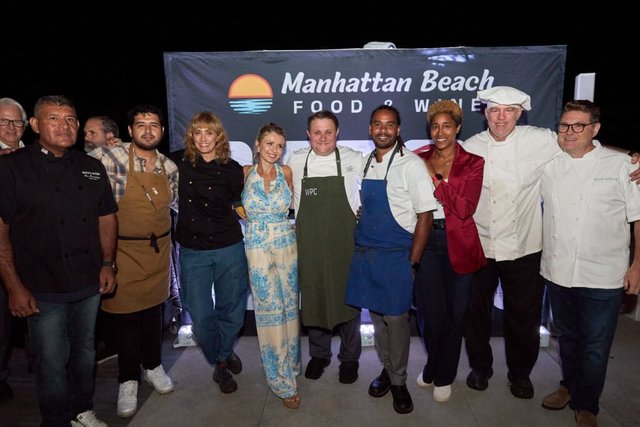 Chefs in aprons and whites pose with guests in front of the Manhattan Beach Food & Wine banner at night