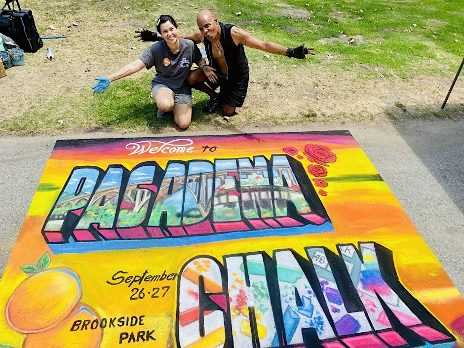 Two chalk artists kneel beside a colorful Welcome to Pasadena Chalk mural drawn on the pavement at Brookside Park