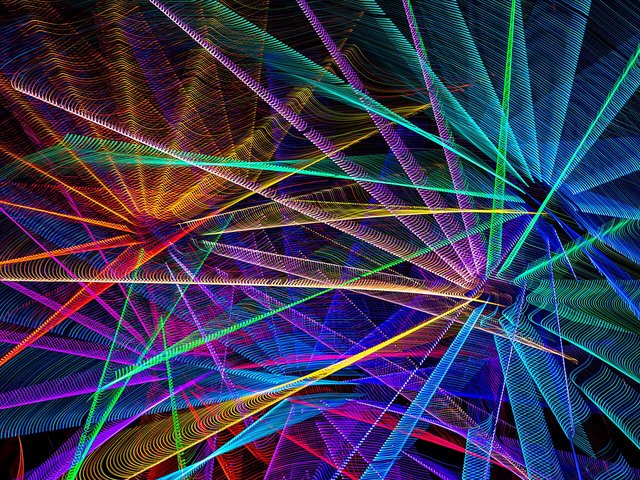 Long-exposure photo of a ferris wheel with rainbow light trails radiating from its spokes against a night sky