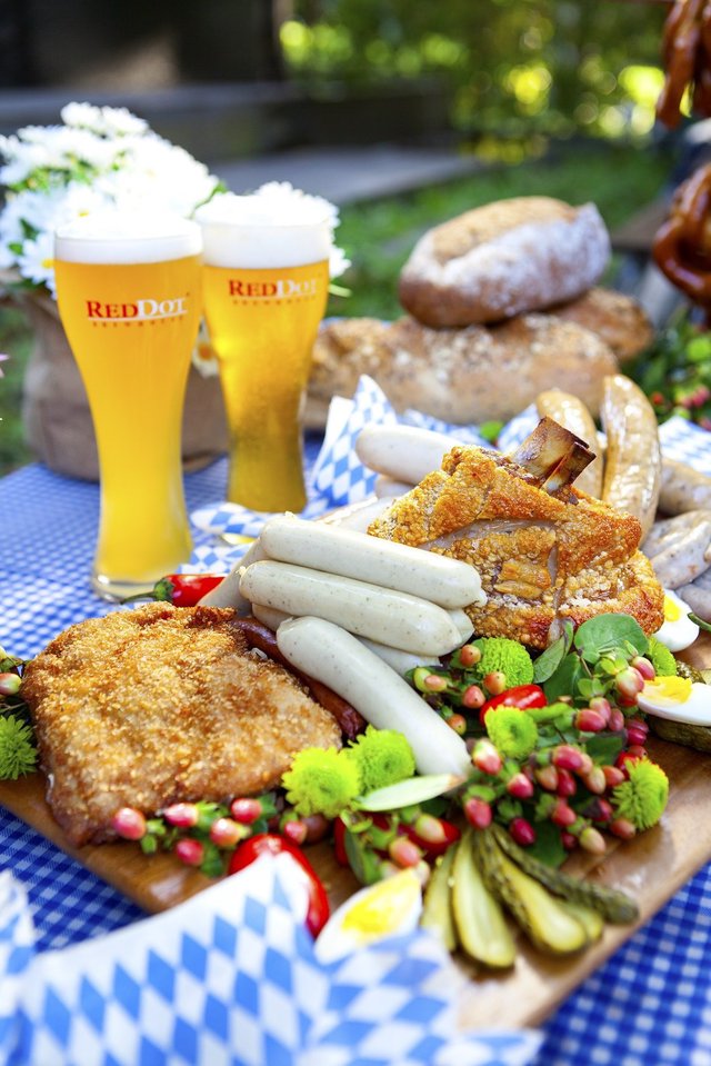 Long table spread with Oktoberfest food including pretzels, sausages, and beer steins at a festive celebration