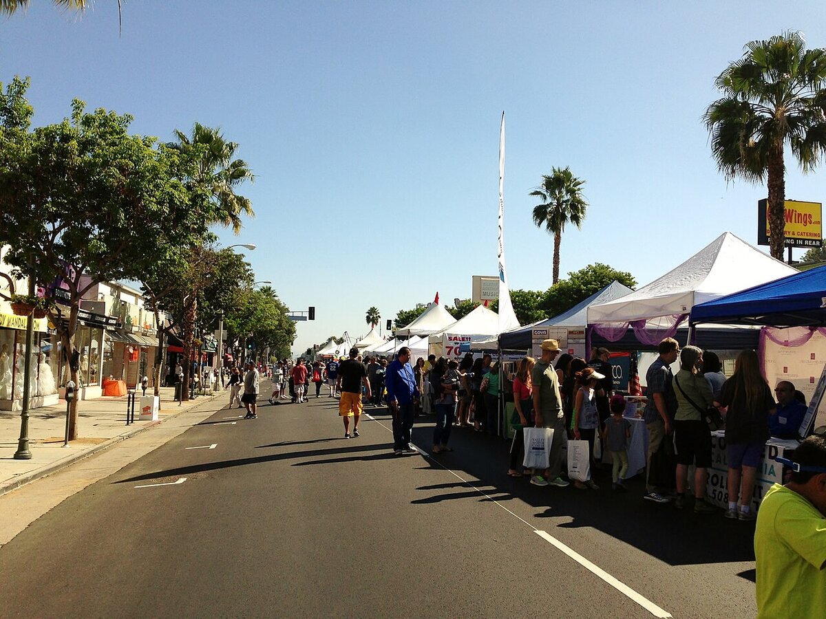 Crowds browsing white vendor tents along a closed-off Ventura Boulevard under palm trees at a past Sherman Oaks Street Fair