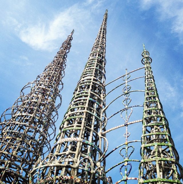 Looking up at the tall mosaic-covered steel spires of Simon Rodia's Watts Towers against a blue sky